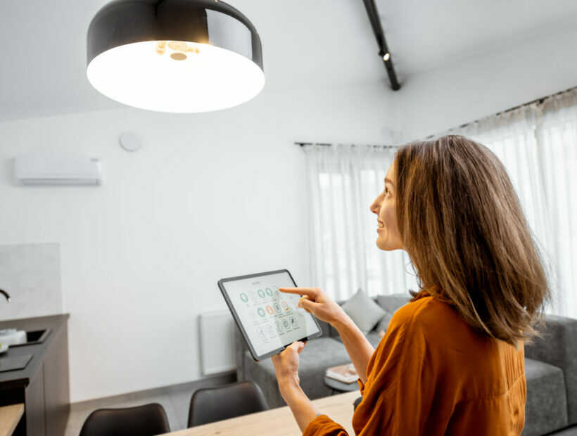 Young woman controlling home light with a digital tablet in the living room. Concept of a smart home and light control with mobile devices